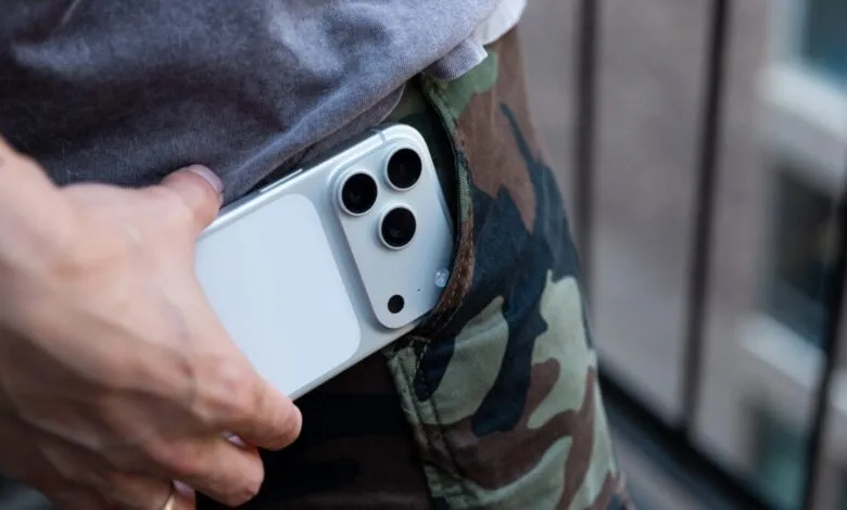 Silver iPhone with triple camera in camouflage pants pocket.