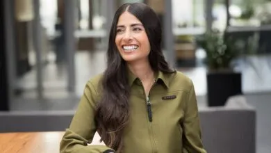 Asha Sharma smiles in an olive green jacket, looking off to the side.