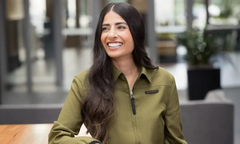 Asha Sharma smiles in an olive green jacket, looking off to the side.