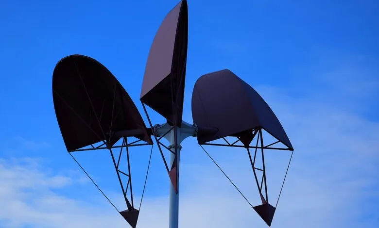 Kinetic wind sculpture with three curved sails against a blue sky.