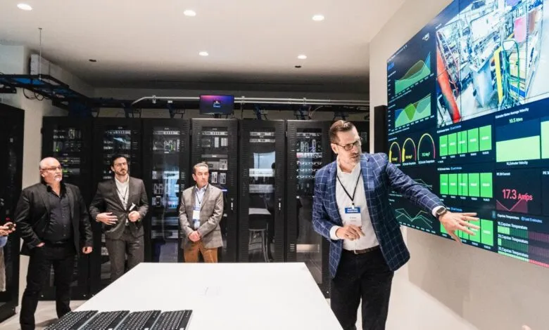 Group of people in a server room looking at a large data display screen.