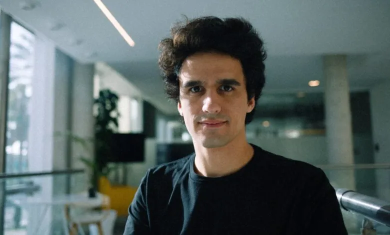Portrait of a man with dark hair and a black shirt smiling slightly.