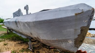 Gray submarine on land, supported by metal stands, near water.