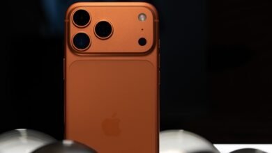 Close-up of an orange iPhone with triple camera system on a dark background.