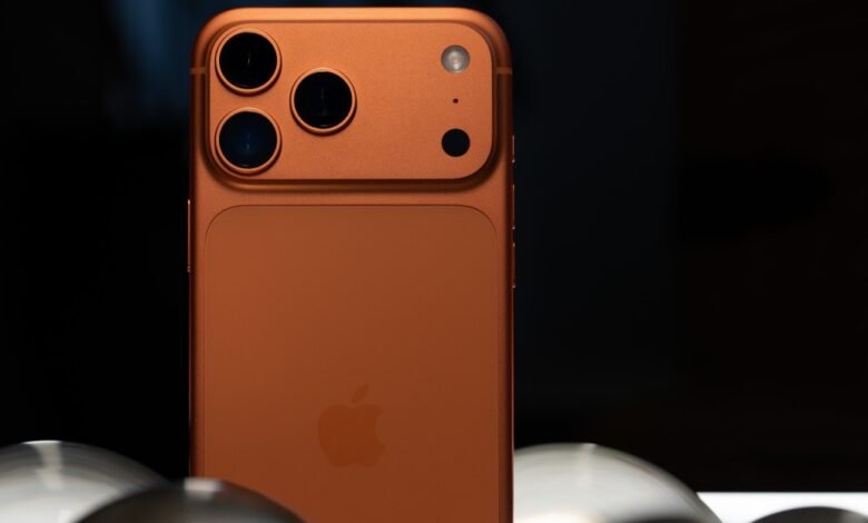 Close-up of an orange iPhone with triple camera system on a dark background.