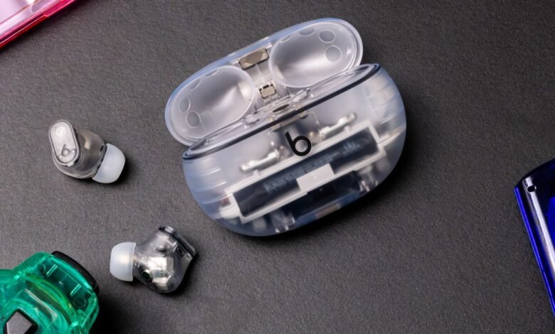 Transparent Beats earbuds and open charging case on a dark surface.