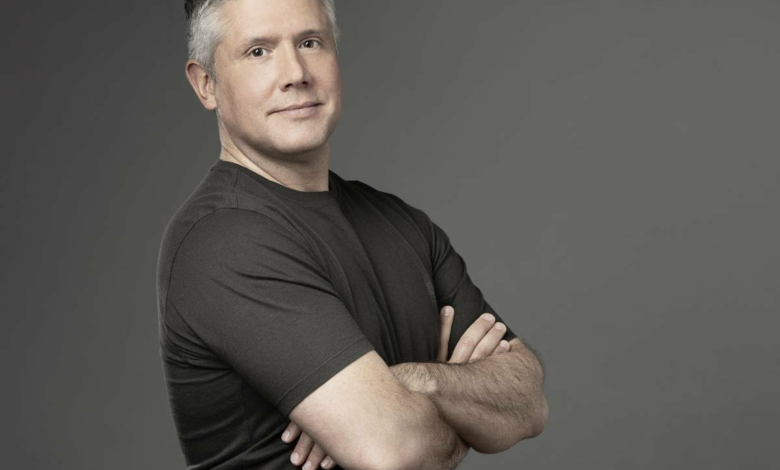 Headshot of actor Darren Mowry with arms crossed, smiling slightly against a gray background.
