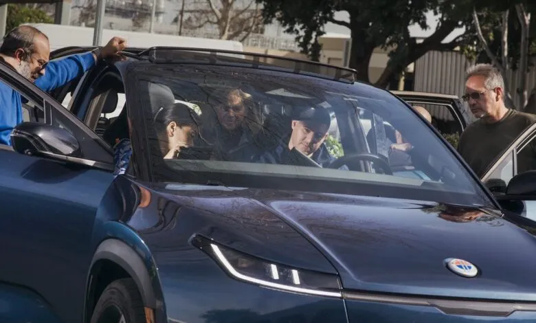 People examining a blue Fisker electric vehicle outdoors.