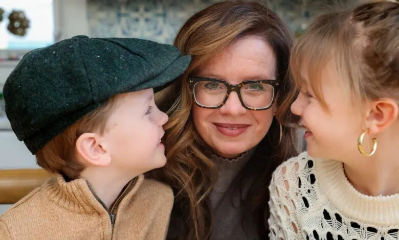 Woman smiles between a young boy in a cap and a girl with gold hoop earrings.