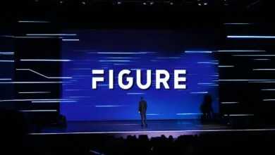 Speaker stands on stage in front of large screen displaying 'FIGURE'.