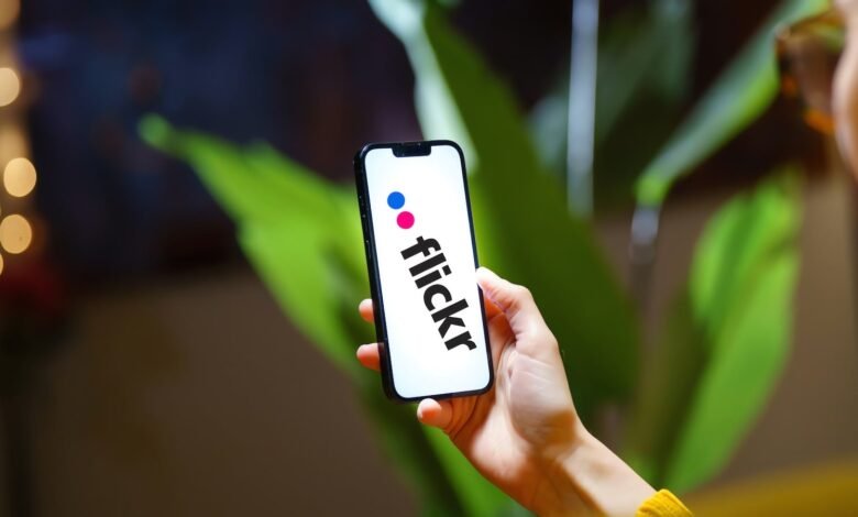 Hand holding smartphone displaying the Flickr logo.
