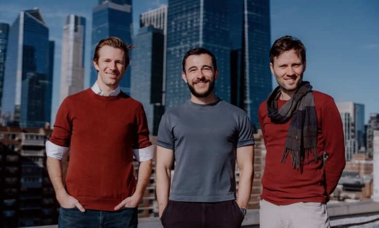 Three men stand smiling against a city skyline backdrop.