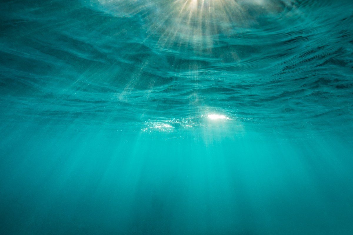 Sunlight streams through turquoise ocean water, creating a serene underwater scene.