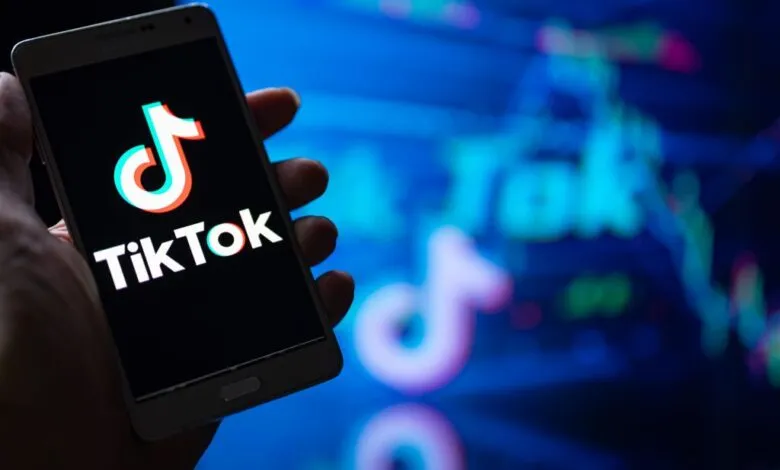 Hand holding smartphone displaying the TikTok logo against a blurred blue background.