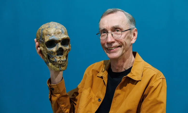 Svante Pääbo holds a Neanderthal skull model against a blue backdrop.