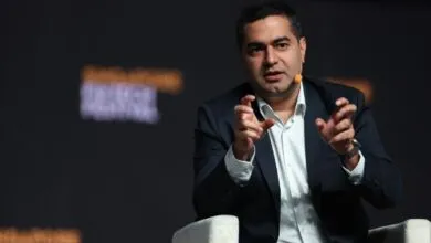 Man in suit gesturing during a presentation on stage.