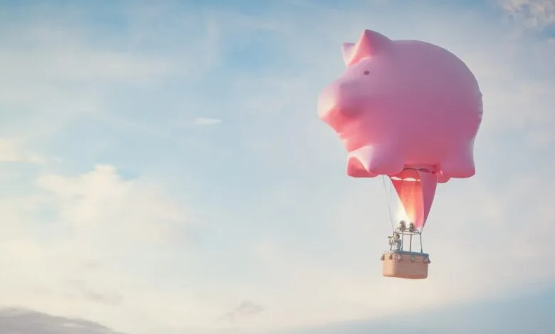 Pink piggy bank hot air balloon floats in blue sky.