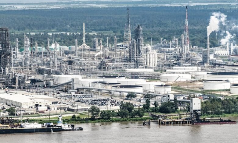 Aerial view of a large industrial oil refinery complex with storage tanks and river.