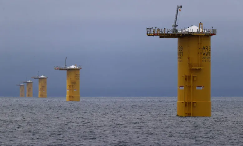 Yellow wind turbine foundations stand in the ocean under a cloudy sky.