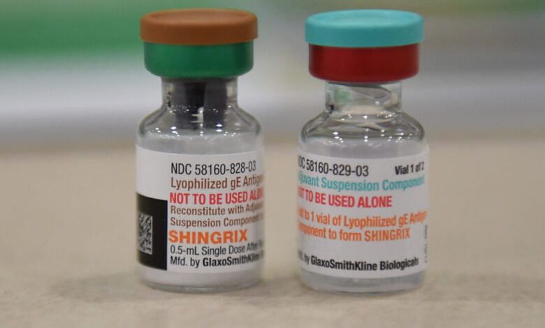 Two vials of Shingrix vaccine with colored caps on a neutral surface.