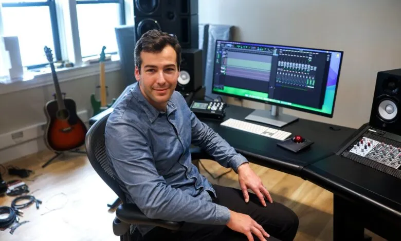 Man sits in music studio with audio equipment and computer screen.