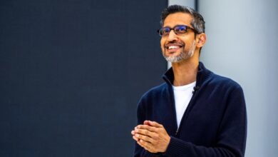 Sundar Pichai smiles warmly with hands clasped in front of a dark background.