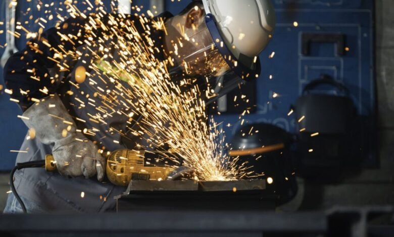 Worker grinding metal with sparks flying, wearing safety gear.