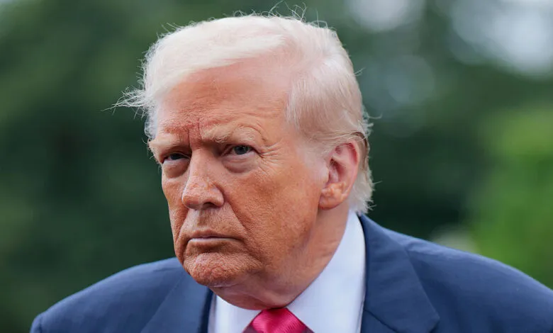 Close-up of Donald Trump in suit and pink tie against green background.