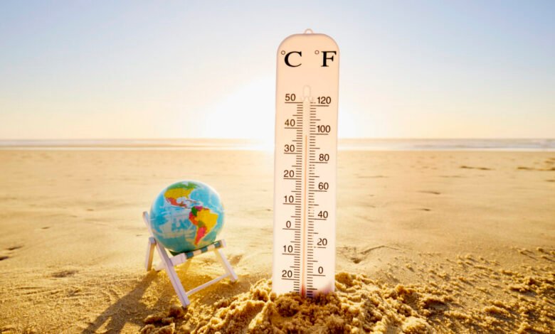 Thermometer in sand next to globe on beach chair, symbolizing climate change.
