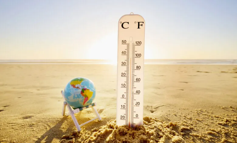Thermometer in sand next to globe on beach chair, symbolizing climate change.