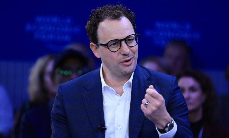 Man in suit speaks at event with audience in background.