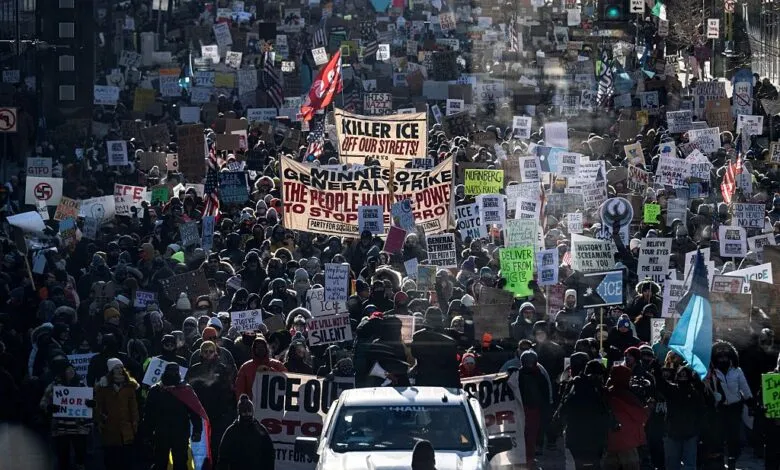 Large crowd protesting ICE with signs and banners in a city street.