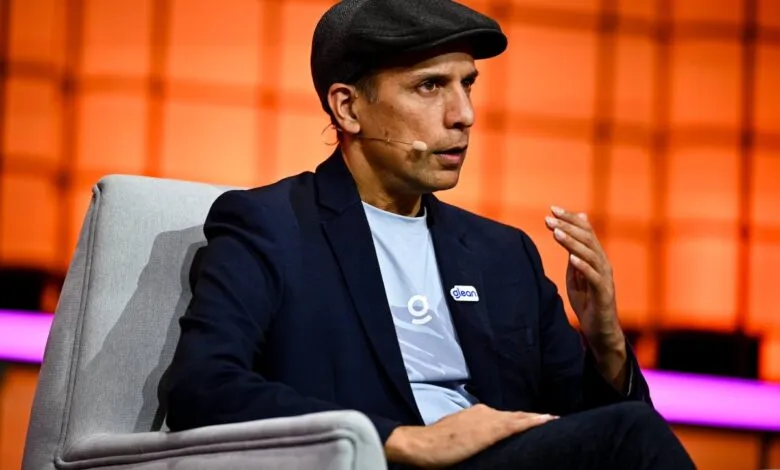 Man in blazer and cap sits in chair, speaking with a microphone.