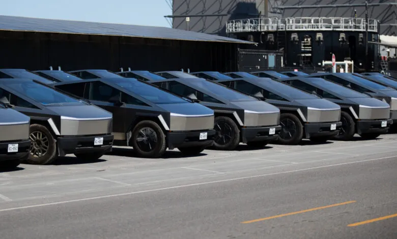 Row of Tesla Cybertrucks parked in front of a large industrial building.