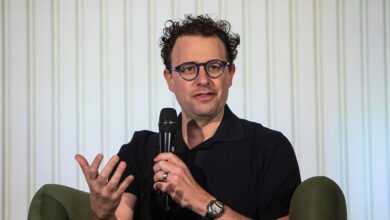 Dario Amodei speaks at event, holding microphone.