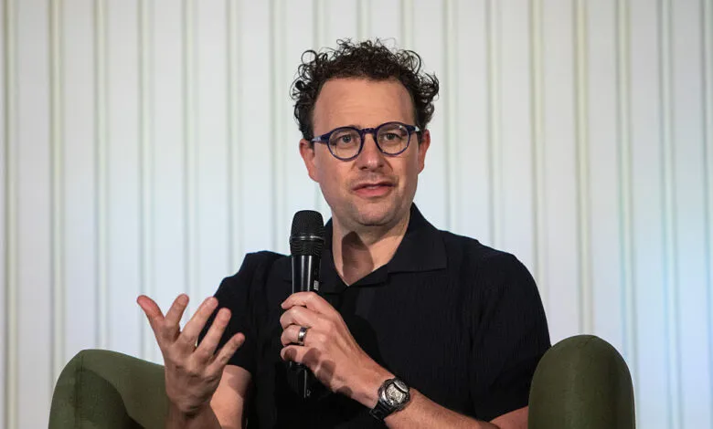 Dario Amodei speaks at event, holding microphone.