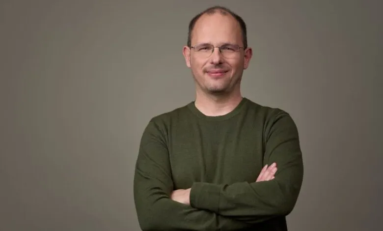 Portrait of a man with glasses and arms crossed, smiling slightly.