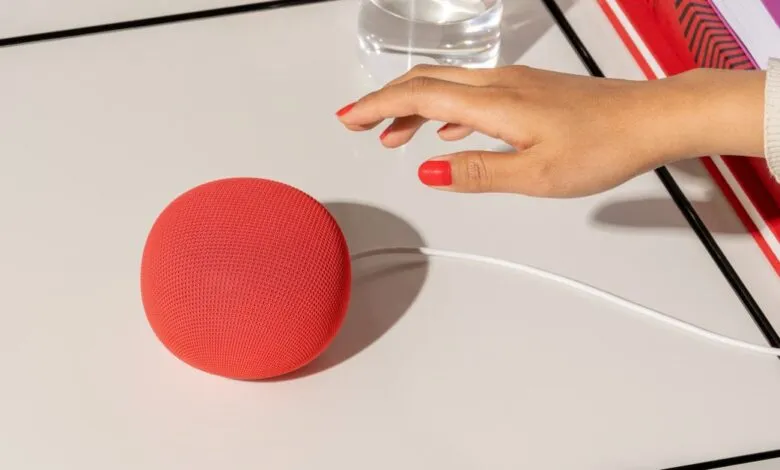 Red Google Nest Mini speaker on a white table with a hand reaching towards it.