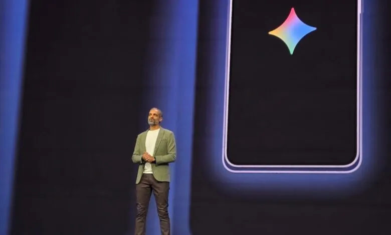 Man presents on stage with large phone display behind him.