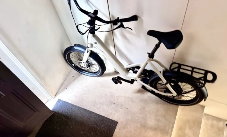 Beige electric bicycle parked indoors against a white wall.