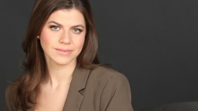 Professional headshot of a woman with brown hair and a blazer against a gray background.