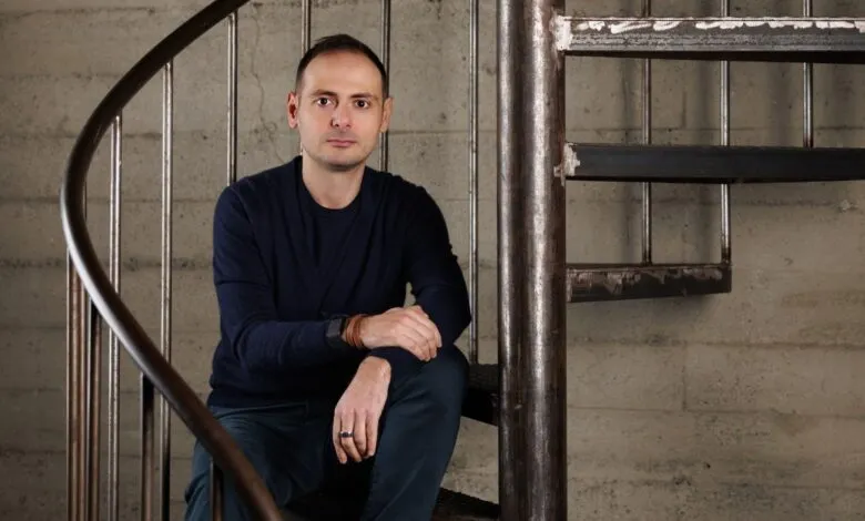 Man in navy cardigan sitting on a metal spiral staircase.
