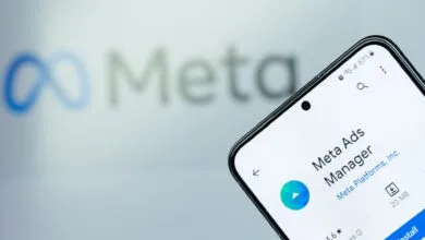Phone displaying the Meta Ads Manager app against a blurred Meta logo background.