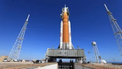 Artemis II SLS rocket on launchpad against clear blue sky.