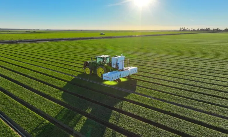 Aerial view of a tractor with laser weeding technology in a green spinach field.