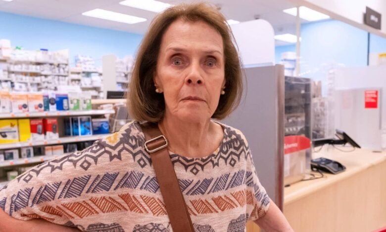 Older woman with shoulder bag stands in a pharmacy.