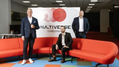 Three men pose in front of Multiverse Computing logo in a modern office setting.