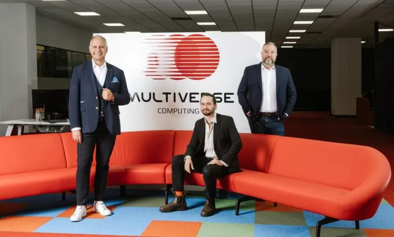Three men pose in front of Multiverse Computing logo in a modern office setting.