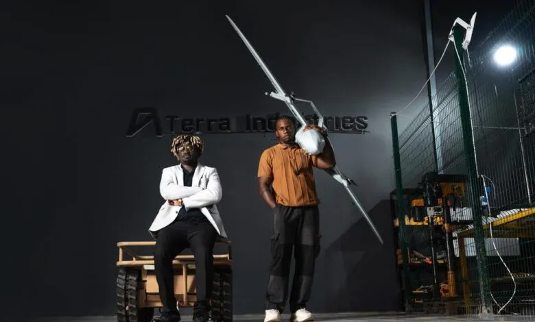 Two men pose with drone in front of Terra Industries logo.