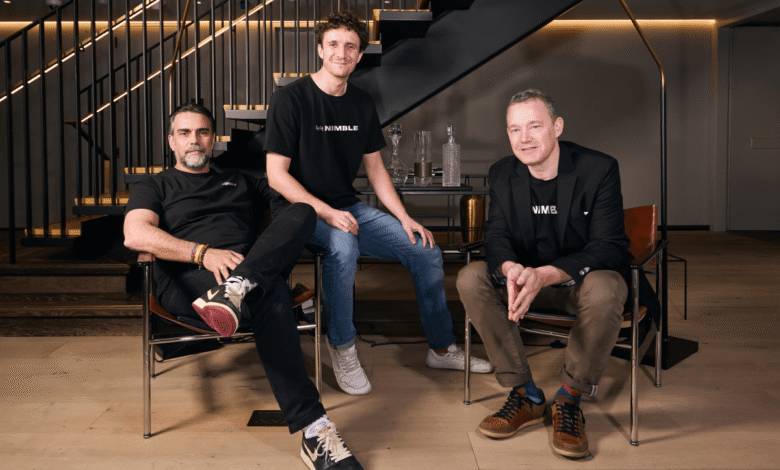 Three men wearing Nimble shirts pose in modern interior with stairs.